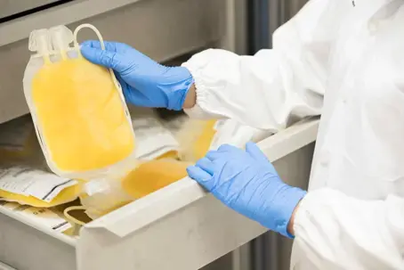 Eine Person mit blauen Handschuhen und einem wei&szlig;en Laborkittel &ouml;ffnet eine Schubalde in der gefrorene Plasmaspendebeutel liegen.