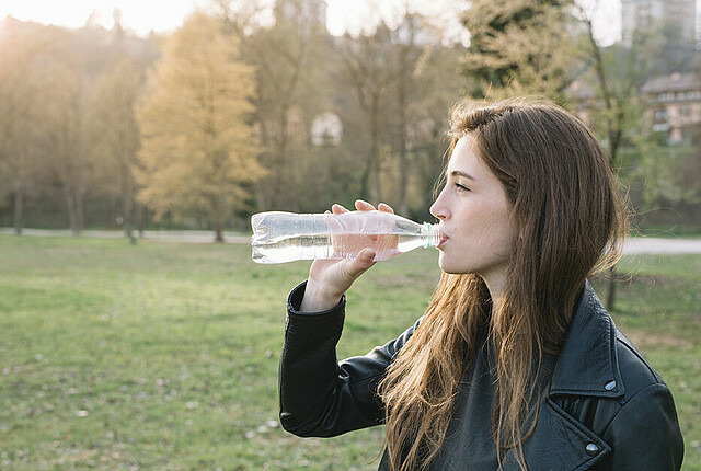 Eine junge Frau steht im Park und trinkt Wasser aus einer Flasche.