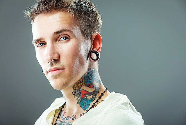 Mann mit buntem Tattoo am Hals und Tunnel-Piercing im Ohr.
